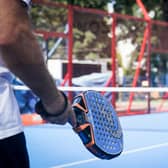 Man standing with a padel racket in an enclosed court. (Credit Unsplash Tomasz Krawczyk)
