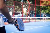 Man standing with a padel racket in an enclosed court. (Credit Unsplash Tomasz Krawczyk)
